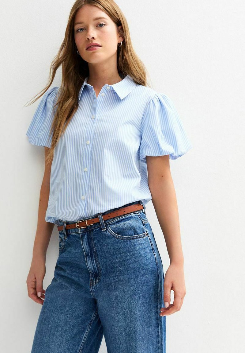 Chemise à rayures bleu clair à manches courtes et à boutons avec un col, associée à un jean bleu taille haute et une ceinture marron.
