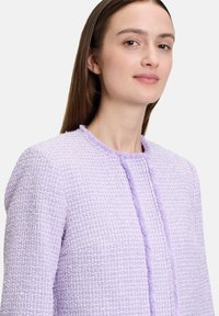 Jasnofioletowa marynarka z tweedu o teksturowym wykończeniu, z okrągłym dekoltem i frędzlami wzdłuż przedniego otwarcia.