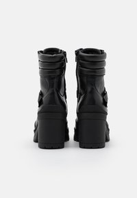 Botas de tobillo de cuero negro con tacón grueso, cuello acolchado y cierre de cremallera lateral. Detalles texturizados notables en la parte trasera.