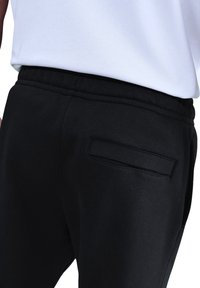 Zwarte joggerbroek van zachte stof, met een elastische tailleband en een enkele opgestikte achterzak.