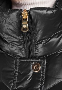 Svart blankt vadderat jacka med guldkedja och rund knapp, båda ingraverade med "RL" initialer på krageområdet.