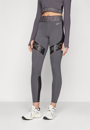 Top corto Nike Pro e leggings grigi scuri con accenti neri. I leggings presentano il marchio e un design aderente ed elegante. Tessuto testurizzato.