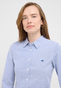 Blue and white striped button-up shirt made of cotton. Features a classic collar and a small embroidered logo on the chest.