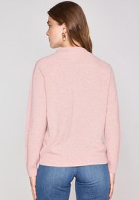 Maglione rosa chiaro realizzato in un tessuto morbido, con un collo alto e polsini a costine, abbinato a jeans in denim blu visibili in vita.