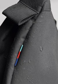 Sac en tissu noir imperméable avec une surface texturée, doté d'une poignée en boucle et de fils colorés en rouge, bleu et vert.