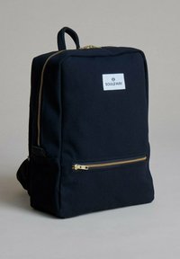 Zaino in tela nera dal design rettangolare, con zip dorate e una tasca frontale. Presenta una patacca con logo bianco sulla parte frontale.