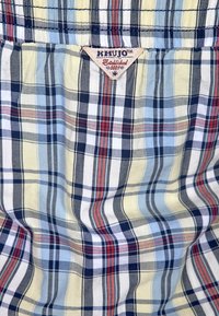 Kostkovaná tkanina s kombinací námořnické, žluté, modré a červené barvy. Měkká textura s etiketou "KHJUO Založeno 2004."