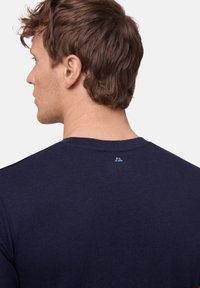 Granatowa koszulka z krótkim rękawem o okrągłym dekolcie. Materiał wydaje się gładki, a z tyłu widać małe logo.