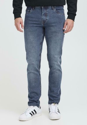 Mørkeblå denimjeans med slim fit, fem-lommers design og subtil falming. Kombinert med hvite sneakers med svarte striper.