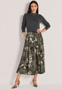 Donkergrijze lange mouwen top met een hoge hals, gecombineerd met een groene bloemenplooien rok en taupe hoge hakken.