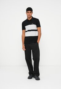 Black and gray striped polo shirt with a solid black bottom, short sleeves, and a small logo on the chest, paired with black loose trousers.