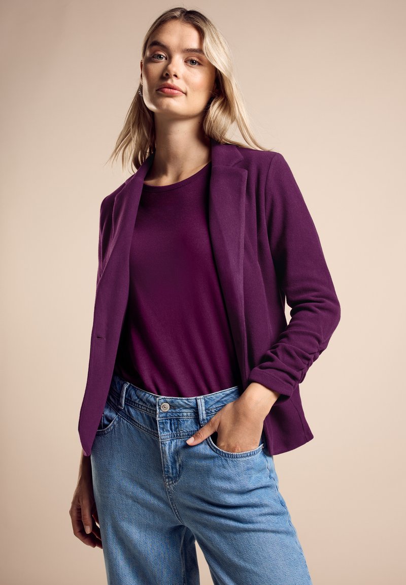 Lila blazer över en lila topp, tillsammans med ljusblå denimjeans. Blazern har en slim fit och en strukturerad design.