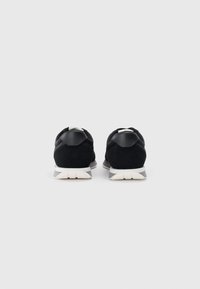 Mustad nahk-sneakerid madala profiiliga, valge põhjaga ja tekstuursete detailidega kandadel. Minimalistlik disain.