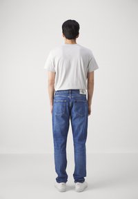 Light gray short-sleeve t-shirt, loose-fit blue denim jeans with back pockets, and white sneakers. Jeans feature a logo tag on the waistband.