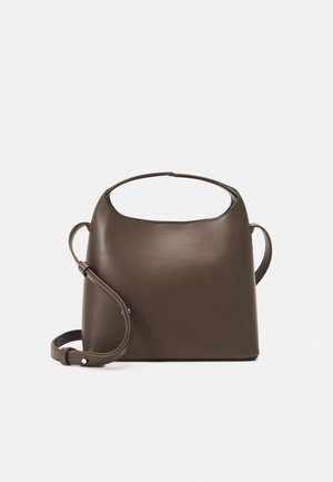 Bruine leren handtas met een gebogen bovenhandvat en verstelbare schouderriem, afgebeeld tegen een effen witte achtergrond.