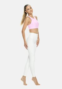 Világos rózsaszín sportmelltartó versenyhátrészes kialakítással és fehér, magas derekú leggings, mindkettő rugalmas anyagból, egy álló modellen bemutatva.