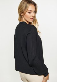 Maglione nero a costine con scollatura rotonda, maniche lunghe e fitting rilassato. Presenta una texture liscia e dettagli di cucitura sottili.