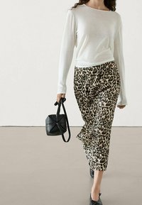 Weißes Langarmoberteil aus leichtem Stoff, kombiniert mit weit geschnittenen Hosen im Leopardenmuster. Eine schwarze Handtasche und passende Schuhe runden den Look ab.