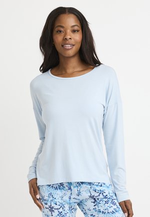 Helles blaue Langarmoberteil aus weichem Stoff mit rundem Halsausschnitt. Kombiniert mit gemusterten blauen und weißen Leggings mit floralen Motiven.