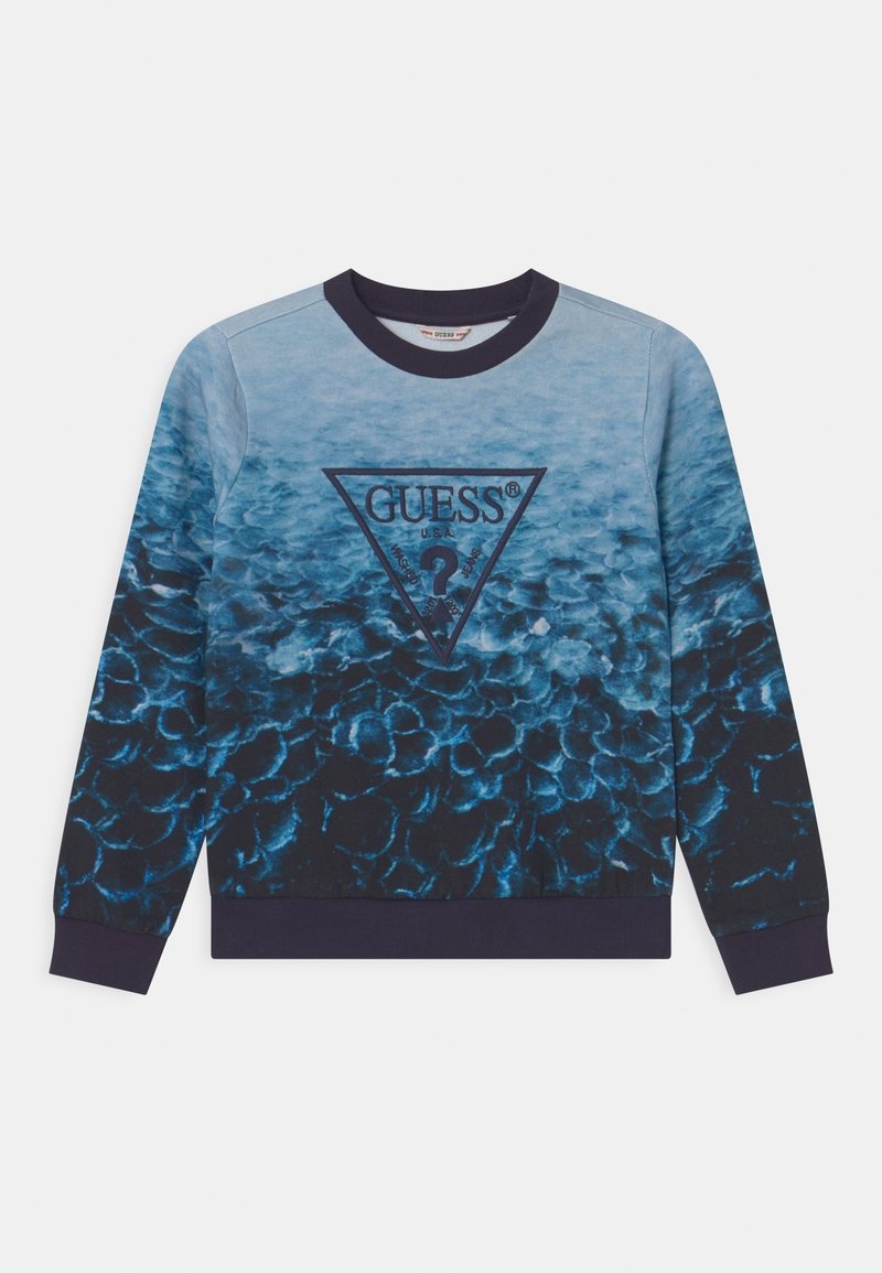 Felpa con gradiente blu che presenta un logo triangolare "GUESS" al centro, un motivo testurizzato che ricorda le squame e polsini a coste blu navy.