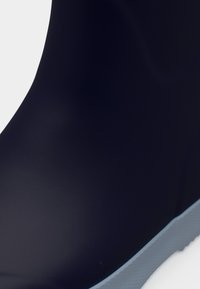 Μπλε ναυτικό λαστιχένιο αδιάβροχο μπότες με ομαλή υφή, διαθέτοντας εξωτερική σόλα σε ανοιχτό μπλε χρώμα και στρογγυλεμένη πρόσθια σχεδίαση.