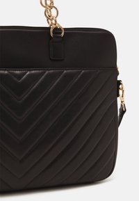 Sort lædertaske med quiltet chevron-mønster, guldfarvede beslag, toplynlås og aftagelig skulderrem.
