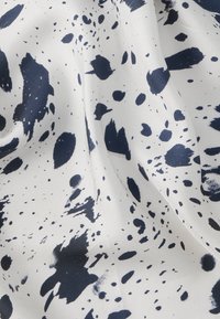 Υφασμάτινο ύφασμα με λευκό φόντο που παρουσιάζει αφηρημένα σχέδια με πιτσιλιές σε ναυτικό μπλε χρώμα. Ομαλή υφή με μοτίβα σε διαφορετικά μεγέθη.