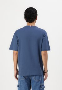 Sininen lyhythihainen T-paita pyöreällä kaula-aukolla, jossa on kontrastivärinen kolmivärinen yhdenmukaisuus takana. Valmistettu pehmeästä puuvillasta, rento malli.