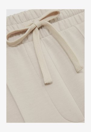 Bež pamučne trenirke s mekom teksturom, s pojasom na vezanje i bočnim džepovima. Glatka tkanina s suptilnim detaljima šivanja.