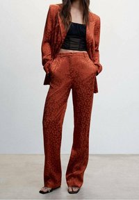 Un costume couleur rouille en tissu lisse, avec un motif de points subtil. Comprend un haut noir ajusté et un pantalon ample avec des poches.