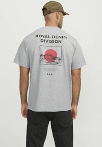 Camiseta de algodón gris con un gran gráfico que muestra un sol rojo y montañas en dibujo lineal. El texto dice "ROYAL DENIM DIVISION" arriba y "R.D.D." abajo.