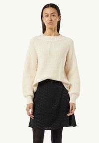 Fleeciger Pullover aus dickem Strick mit gerippter Textur und weiten Ärmeln, kombiniert mit einem schwarzen Rock, der ein dezentes Hahnentrittmuster aufweist.