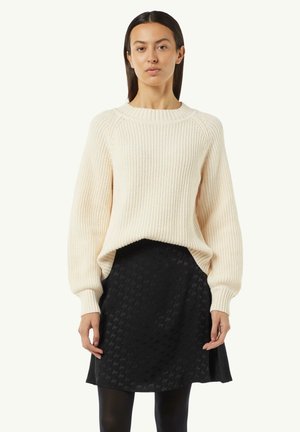 Chunky cream knit sweater with ribbed texture and wide sleeves, paired with a black skirt featuring a subtle houndstooth pattern.