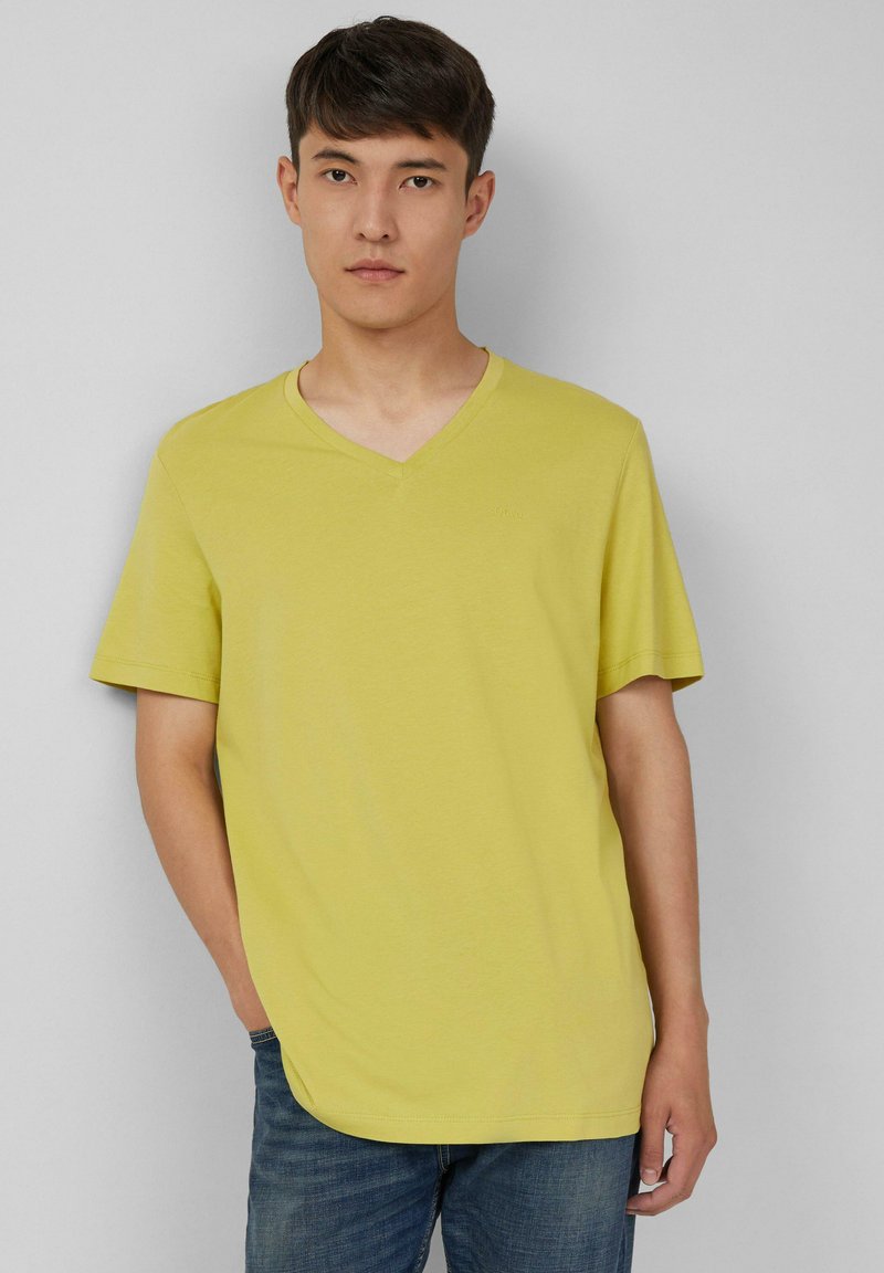 T-shirt jaune à manches courtes et col en V, fabriqué en tissu doux, avec une coupe décontractée et un logo discret sur la poitrine. Assorti à un jean bleu.