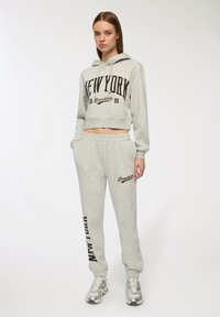 Jasnoszara skrócona bluza z kapturem z grafiką "NEW YORK", zestawiona z dresami w tym samym kolorze z napisem "BROOKLYN" i elastycznym pasem.