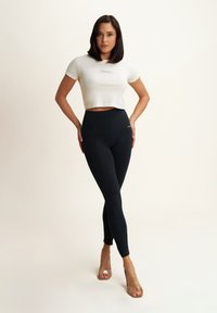 Leggings neri con vita alta, abbinati a una maglietta bianca corta con un piccolo logo. Sandali trasparenti con tacco completano l'outfit.