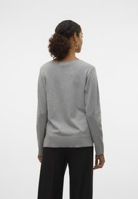 Pull en coton gris à manches longues, avec un col rond, un ourlet côtelé et une texture lisse. Porté avec un pantalon noir à larges jambes, vu de dos.