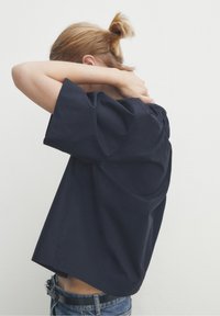 Top blu navy a maniche corte con vestibilità rilassata e dettaglio plissettato sul retro. Tessuto dalla texture morbida. Indossato con jeans in denim.