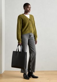 Μαύρη τσάντα ώμου με δύο λαβές, υφασμάτινο γκρι πουλόβερ από μαλλί, λευκό πουκάμισο, γκρι τζιν και μαύρες γαλότσες με τακούνι.