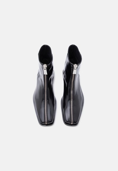 Ζευγάρι μαύρα γυαλιστερά δερμάτινα μποτάκια με ασημένια φερμουάρ μπροστά και τετράγωνα δάχτυλα σε λευκό φόντο.