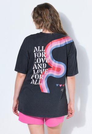 Osoba o falowanych włosach nosi czarną koszulkę z napisem "Wszystko dla miłości i miłość dla wszystkich" oraz kolorowym wzorem fal, w połączeniu z jasnoróżowymi szortami.