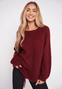 Burgundowa dzianinowa sweter z luźnym krojem, szerokimi rękawami i ściągaczem u dołu. Miękka tekstura, wycięcie typu crew oraz minimalne detale.