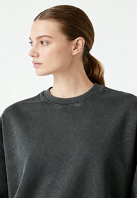 Tumehall crewneck-sweater tekstureeritud kangaga, soonikuga krae ja lõdva lõikega, kujutatud profiilis mudelil heledal taustal.