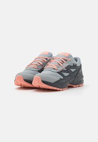 Zapatillas grises y gris oscuro con acentos en rosa, materiales de malla texturizada y goma, que presentan un diseño moteado y una puntera reforzada.