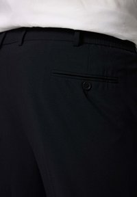 Schwarze Hosen mit strukturiertem Finish, einer einzigen Gesäßtasche mit Knopfverschluss und Gürtelschlaufen an der Taille.