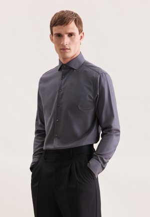 Heren overhemd met lange mouwen in marineblauw met een klein wit ruitpatroon, button-down kraag en zachte stof. Gepaarde met getailleerde zwarte broek.