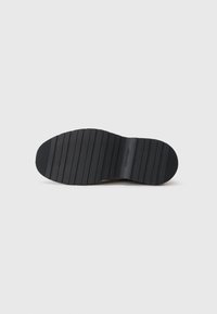 Semelle de chaussure en caoutchouc noir avec des rainures horizontales, arborant un nom de marque en relief, conçue pour l'adhérence et la durabilité.