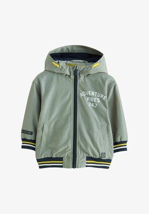 Una giacca leggera verde con cappuccio, cerniera frontale, testo stampato "ADVENTURE VIBES 24.7" e accenti a righe blu navy-giallo sui polsini.