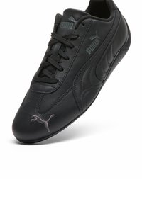 Baskets en cuir noir Puma avec lacets noirs, logos Puma sur la languette, le côté et le bout, inclinées sur fond blanc.