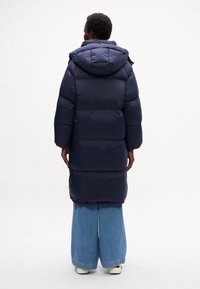 Cappotto imbottito blu navy con cappuccio, caratterizzato da sezioni a righe orizzontali, maniche lunghe e una vestibilità ampia, abbinato a pantaloni in denim a gamba larga.